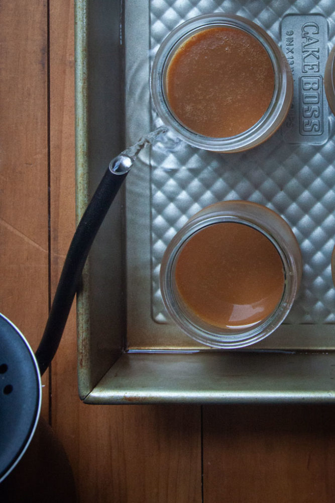 Hot water pouring into a baking pan with caramel pots de creme in them.