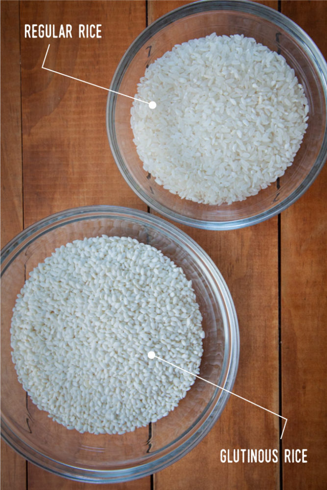Two bowls of raw rice, the top bowl holding regular rice that is slightly translucent, the bottom bowl holding the glutinous rice which is brighter white and opaque.