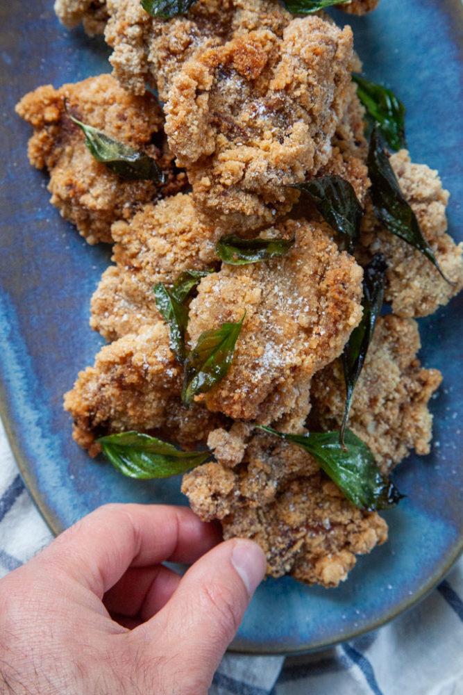 A hand reaching for a piece of Taiwanese popcorn chicken on a plate piled with the chicken.