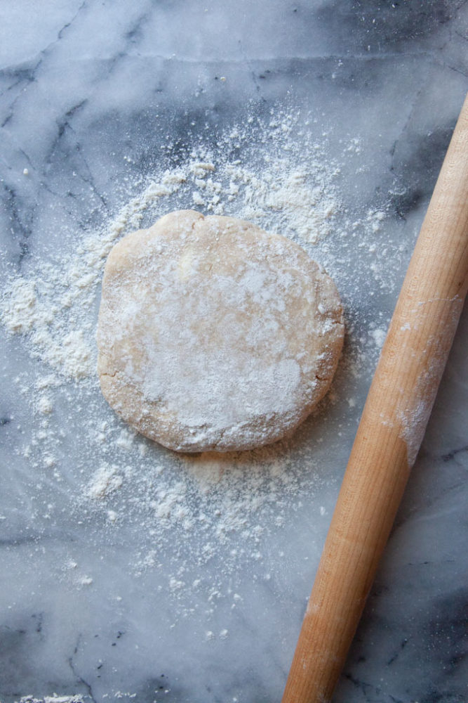A disk of pie crust on a marble counter with a rolling pin next to it.