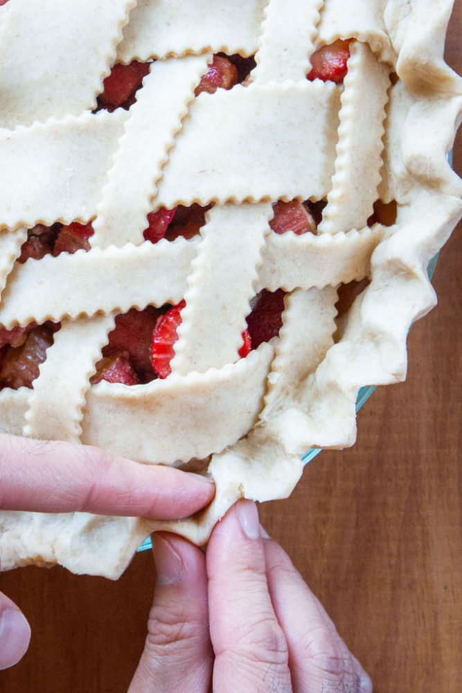 Fingers pressing the crust together at the edges of a pie.