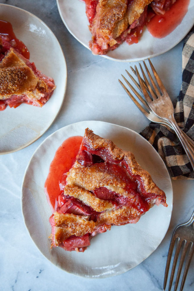 Strawberry rhubarb pie slices on a white plates with forks next to them.
