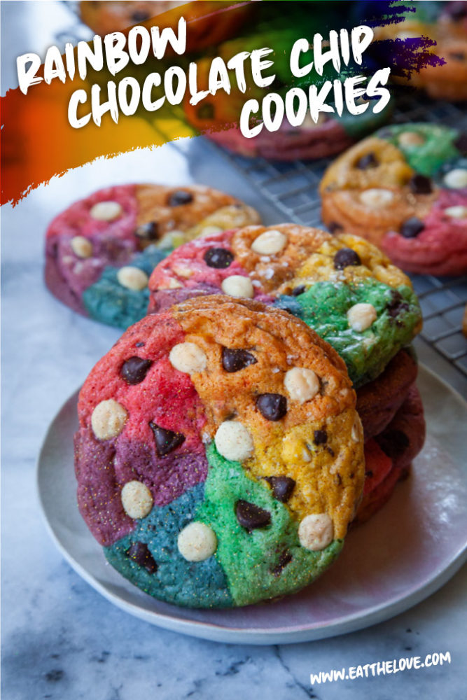 Rainbow chocolate chip cookies on a plate, with more cookies behind it.