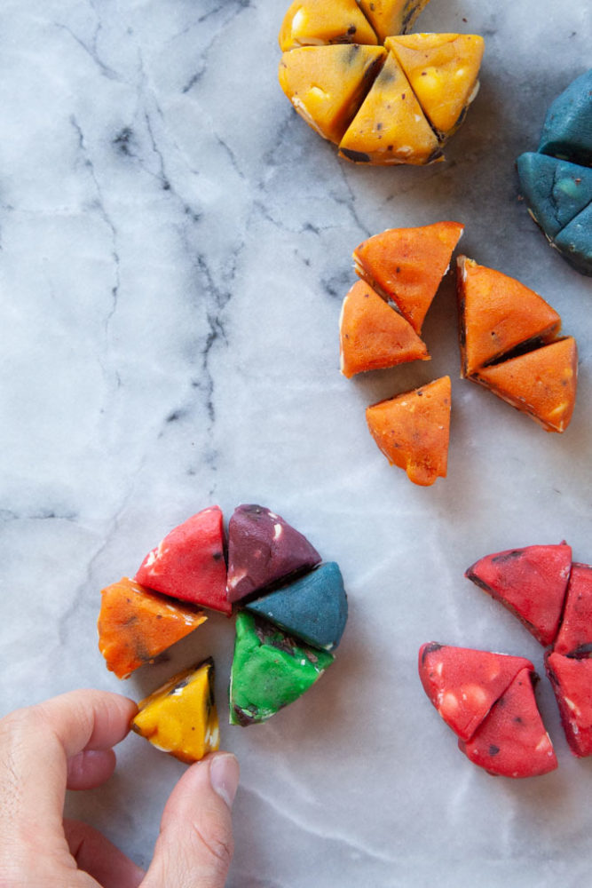 A hand assembling the colored pieces of cookie dough to make the rainbow cookie.