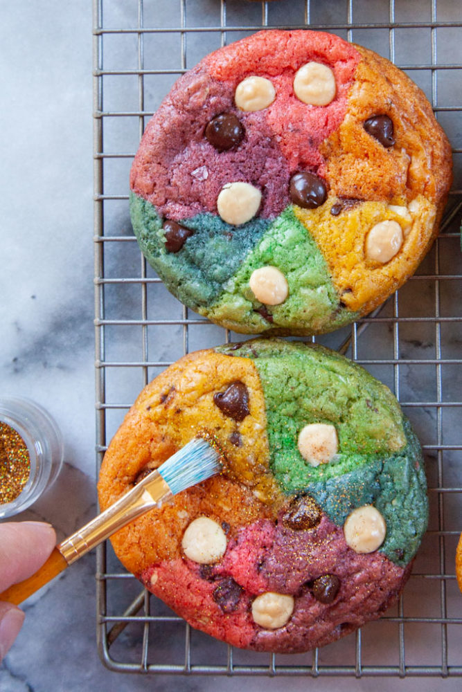 A brush adding edible glitter to a rainbow cookie.