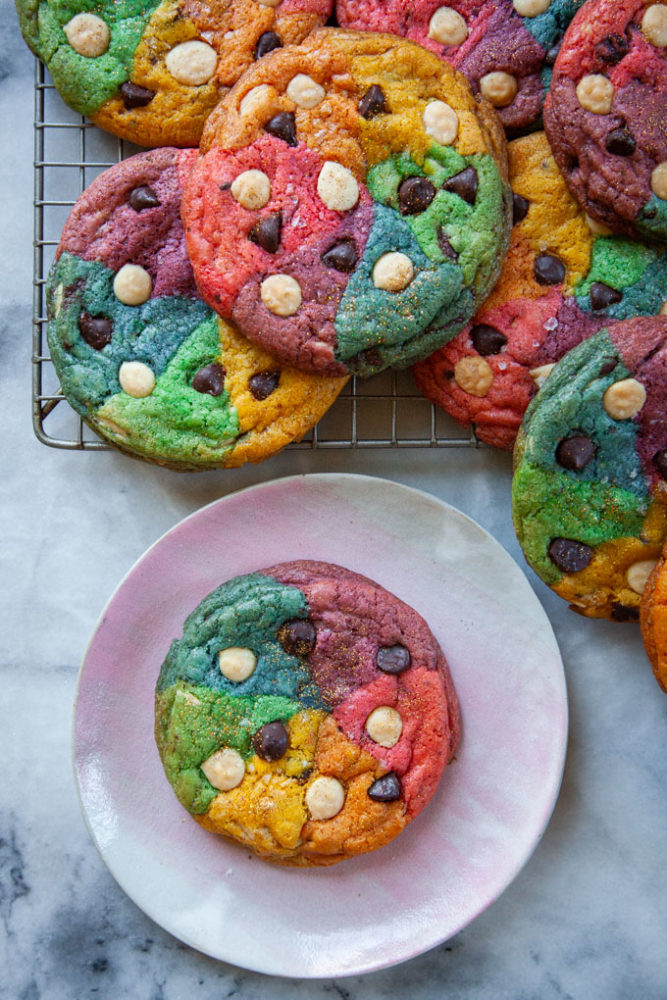 A rainbow cookie on a pink plate with more cookies cooling on a wire rack next to it.