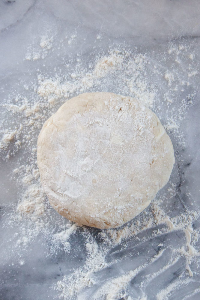 A disk of pie dough on a marble surface dusted with flour.