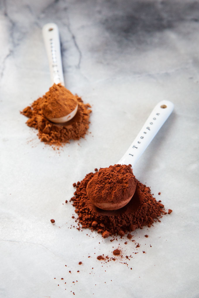 Two spoonfuls of different cocoa powder on a marble surface, with darker Dutch-processed cocoa in front, and natural cocoa powder in back.