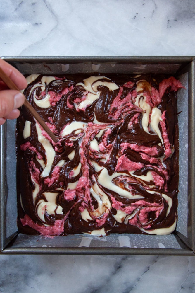 A hand using a chopstick to swirl together batter for a Neapolitan brownie.