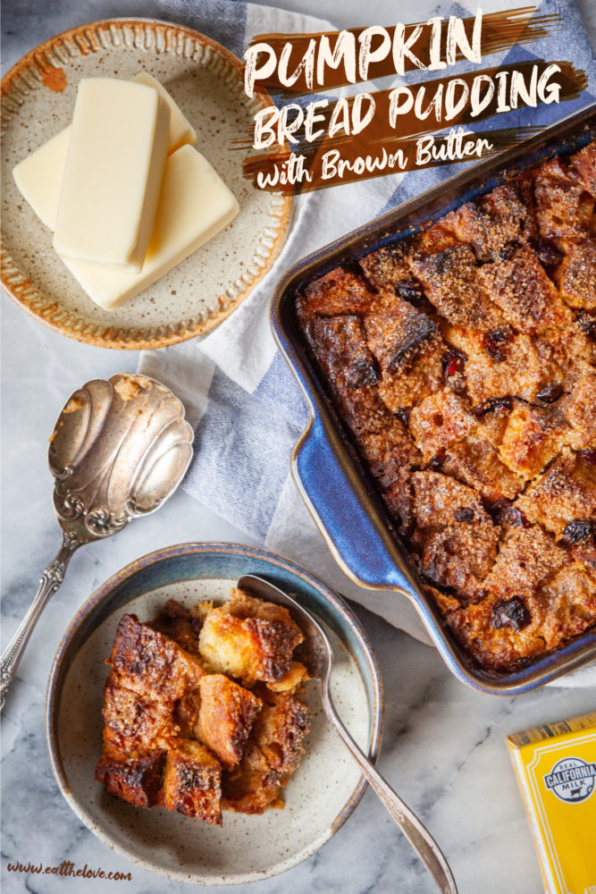 A bowl of pumpkin bread pudding with a pan of more bread pudding and a plate of butter sticks near it.