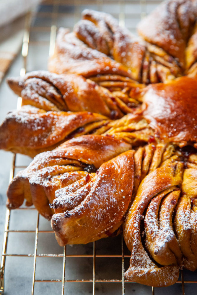 A pumpkin star bread with dried cranberries filling sitting on a gold wire cooling rack.