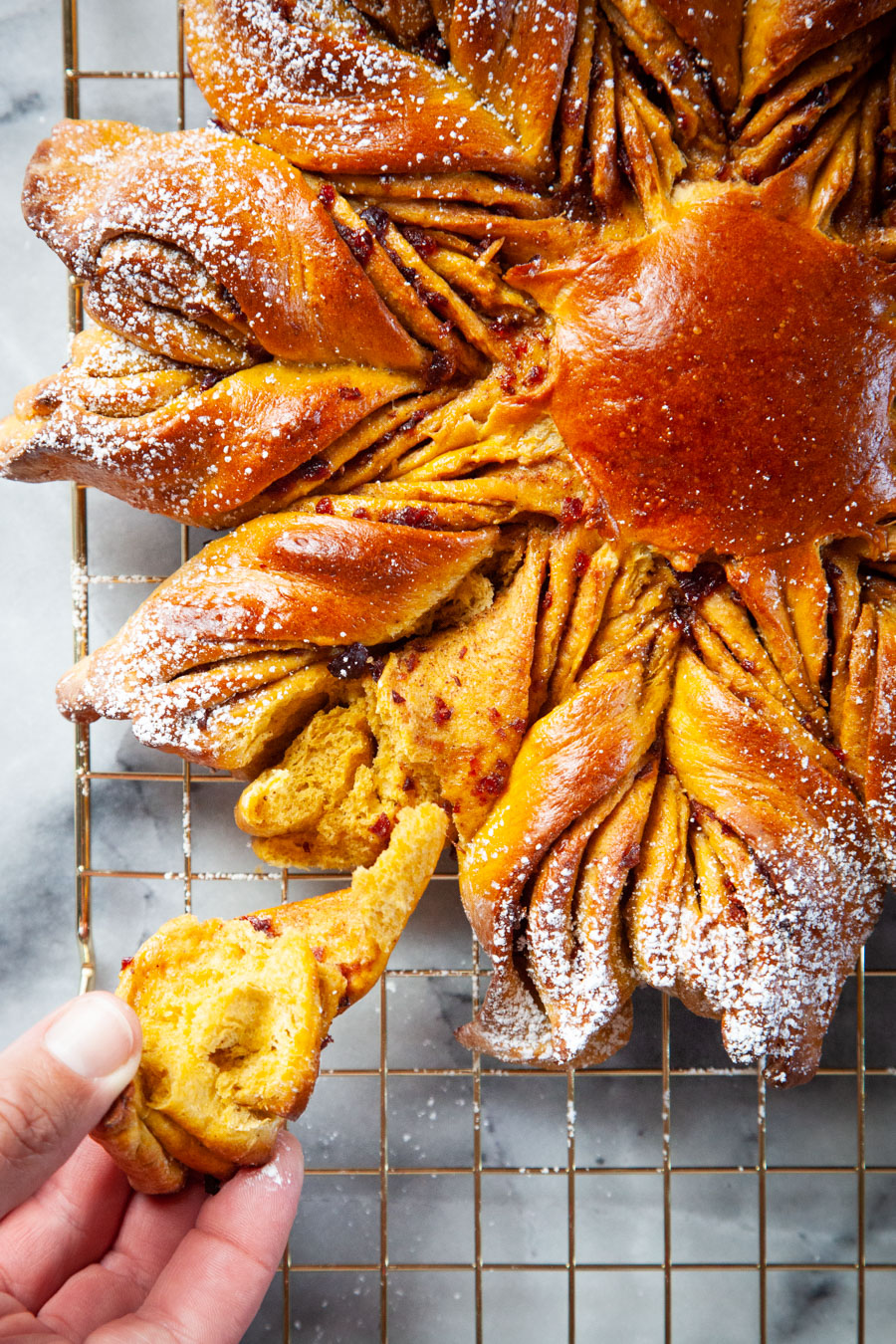 A hand pulling a piece of the pumpkin star bread off.