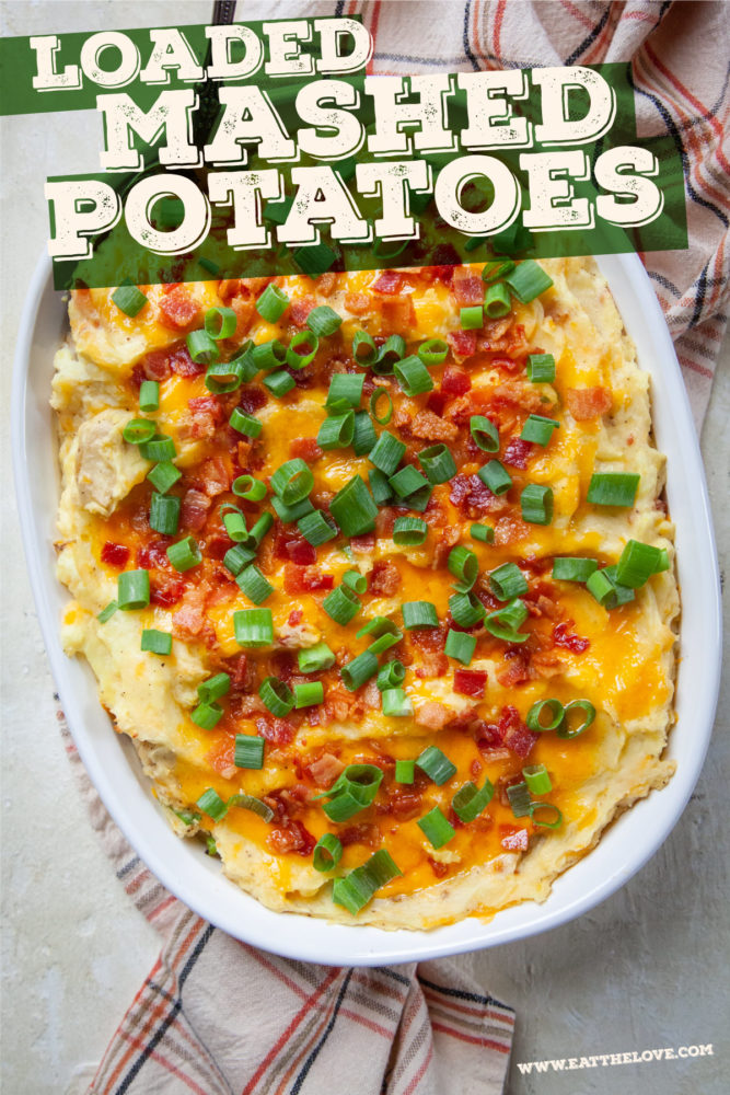 A casserole dish of loaded mashed potatoes sitting on a kitchen towel.