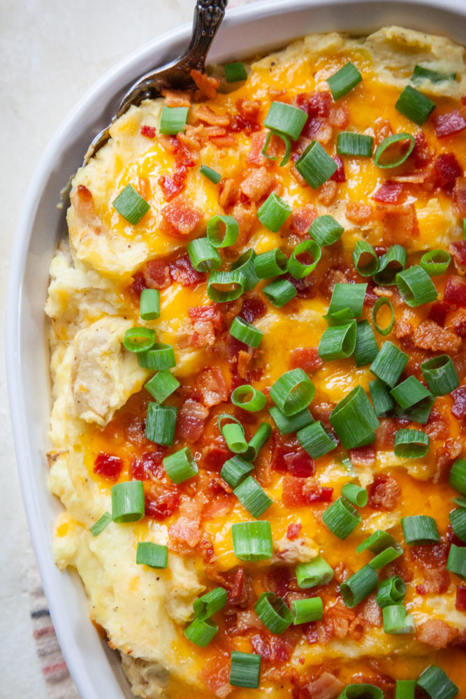 A close up shot of a casserole dish filled with loaded mashed potatoes.