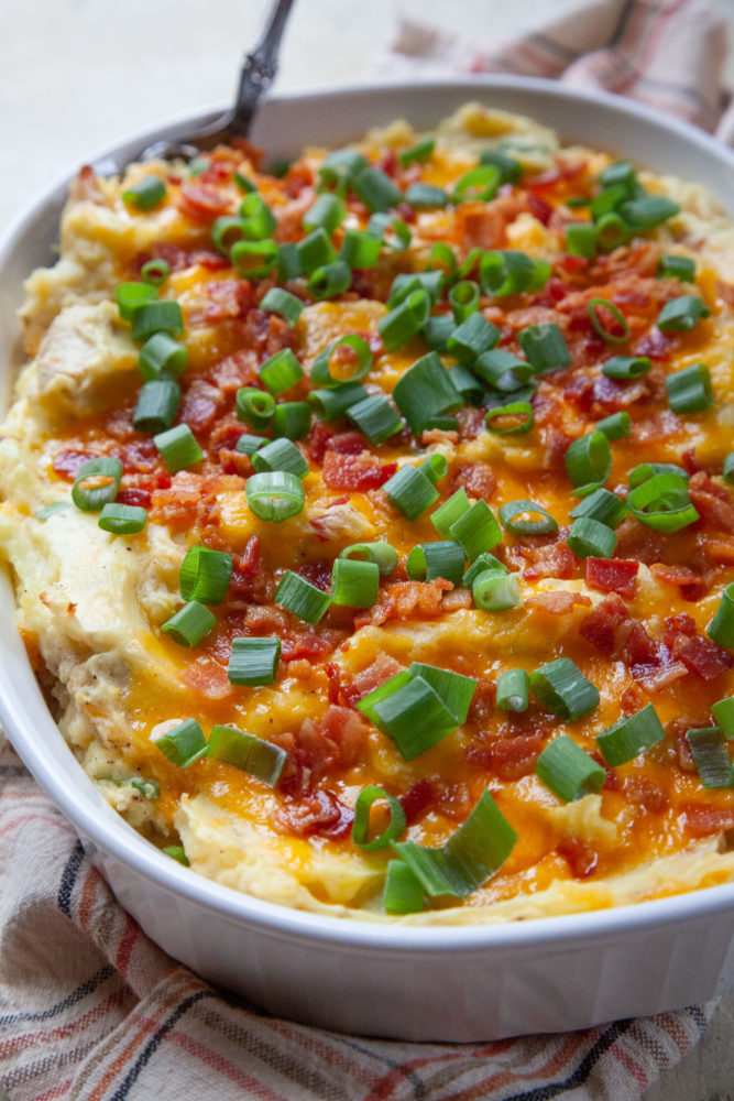 A casserole dish of loaded mashed potatoes sitting on a kitchen towel.