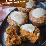 A pumpkin cream cheese muffins broken in half with more whole muffins next to it on a black oval plate.
