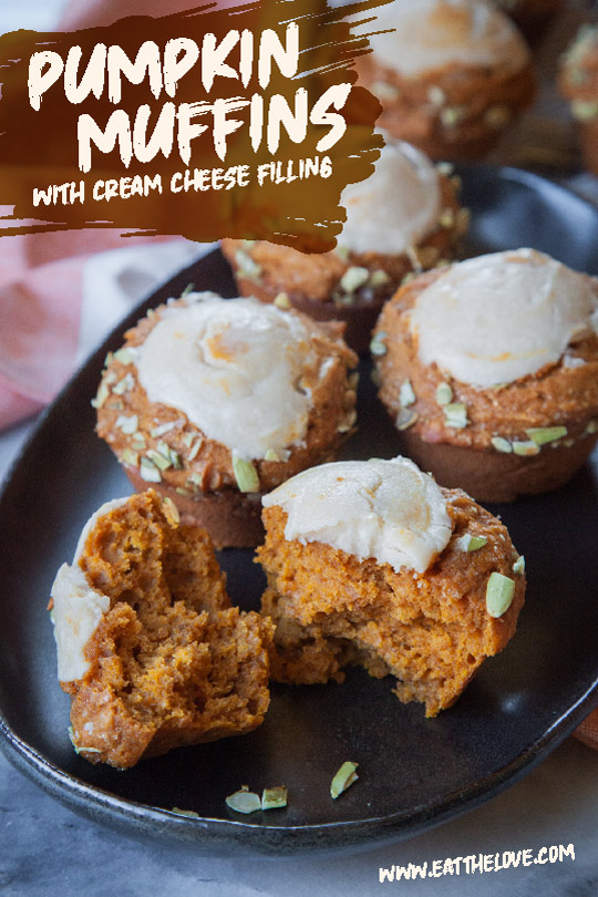 A pumpkin cream cheese muffins broken in half with more whole muffins next to it on a black oval plate.