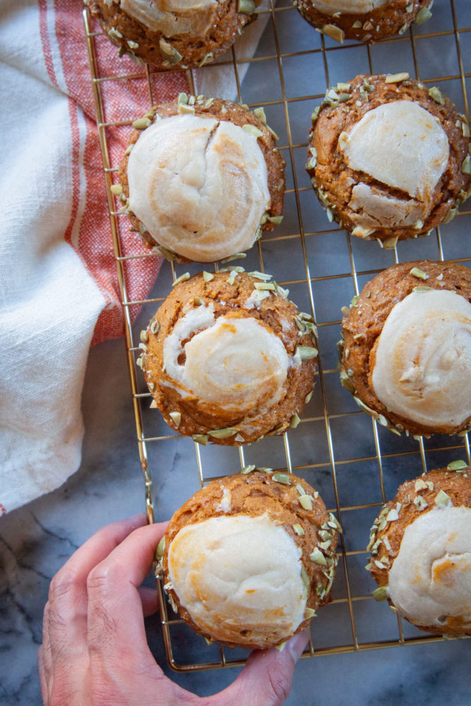 A hand reaching for one of many pumpkin cream cheese muffin resting on a wire cooling rack.