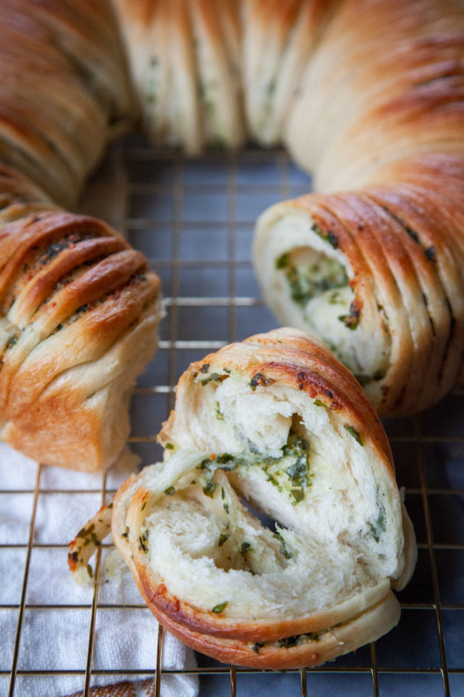 Herb wool roll bread pulled apart, with a piece showing the fluffy interior and the herbs inside the bread.