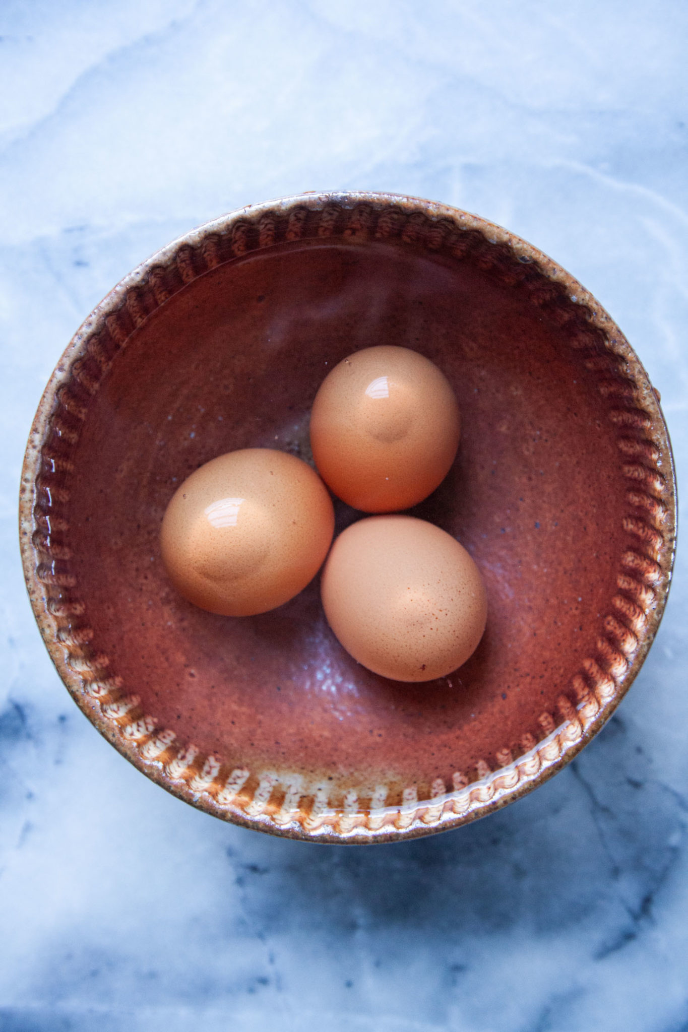 Three eggs sitting in a bowl of hot water.