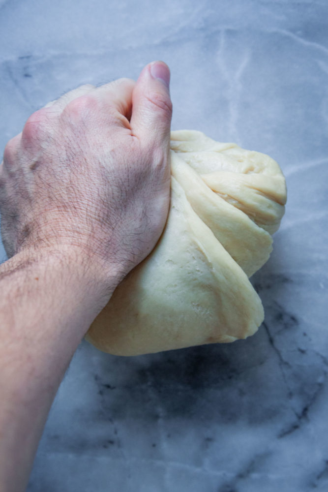 A hand kneading the dough on a marble surface.