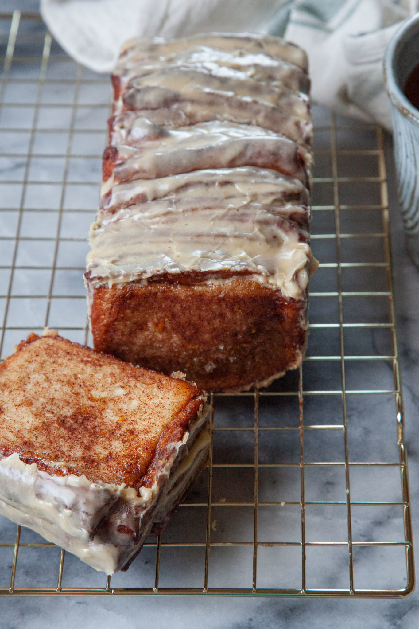 A loaf of cinnamon pull apart bread, with a piece pulled off, sitting on a wire cooling rack.