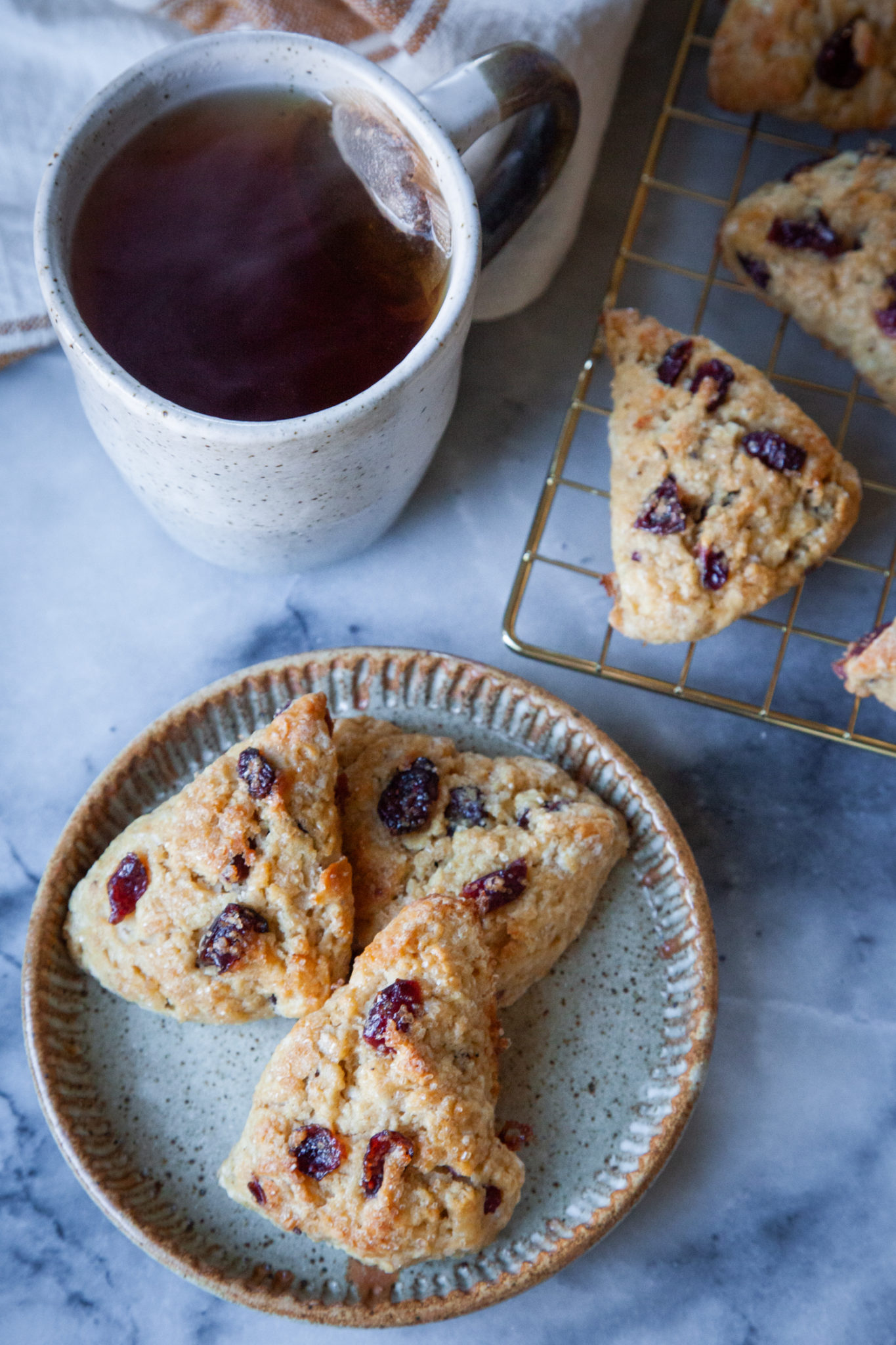 A plate of mini eggnog scones next to a cup of tea and a wire cooling rack with more scones on it.