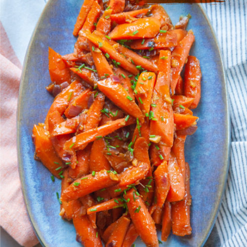 A blue plate of miso glazed carrots topped with chopped green chives.