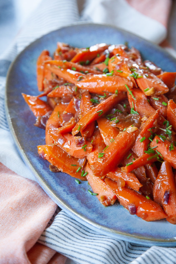 A blue plate of miso glazed carrots topped with chopped green chives.