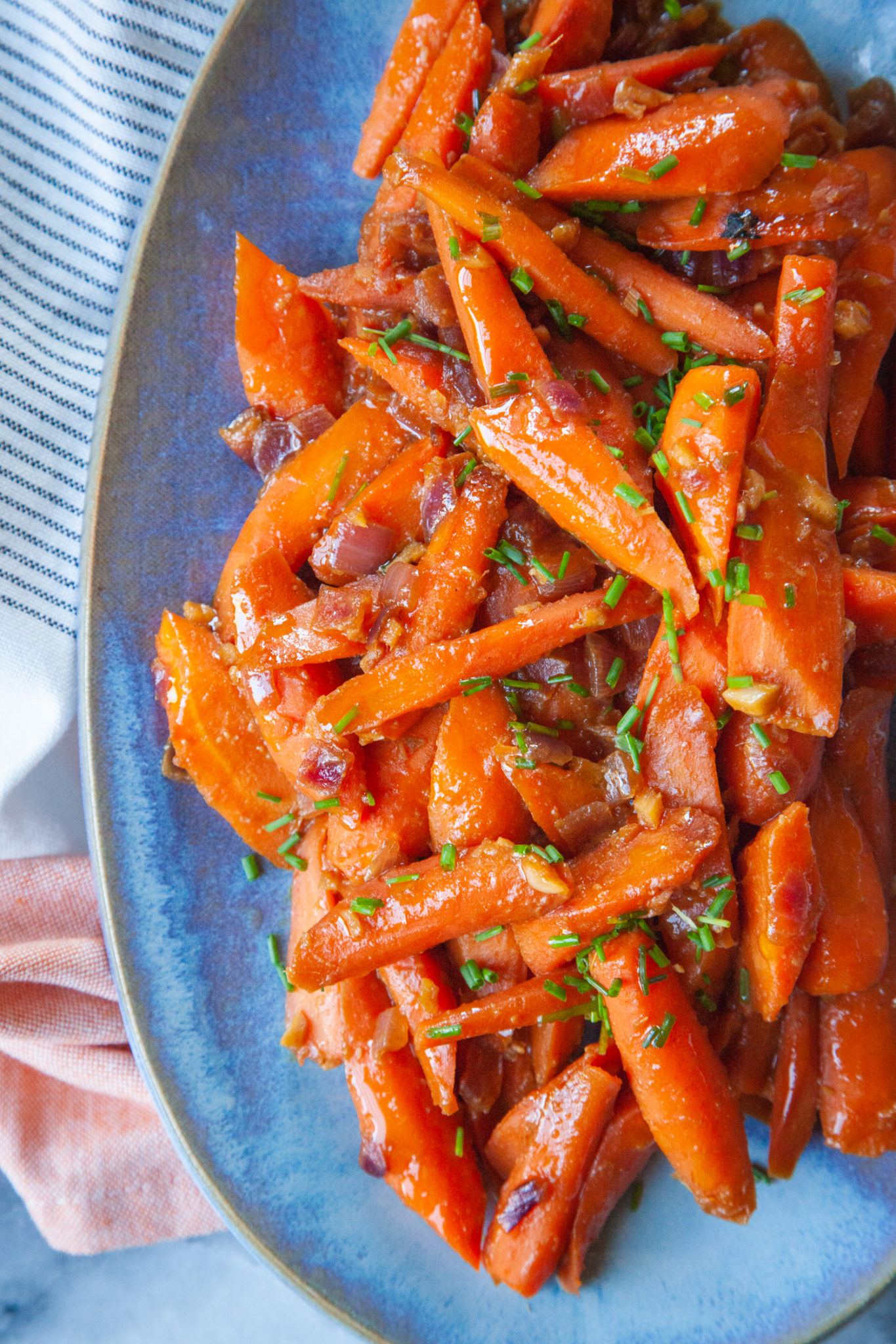 A blue plate of miso glazed carrots topped with chopped green chives.