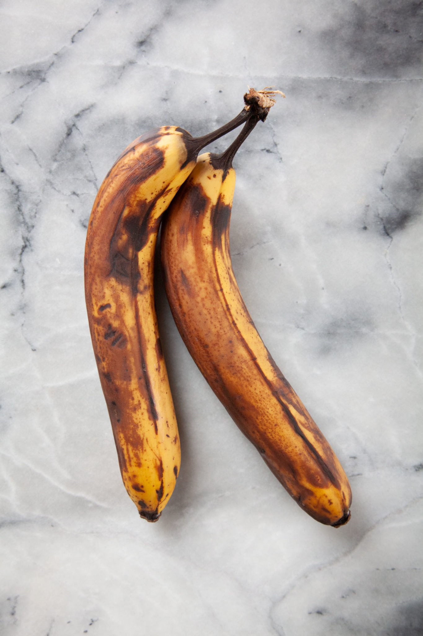 Two overly ripe bananas on a marble surface.
