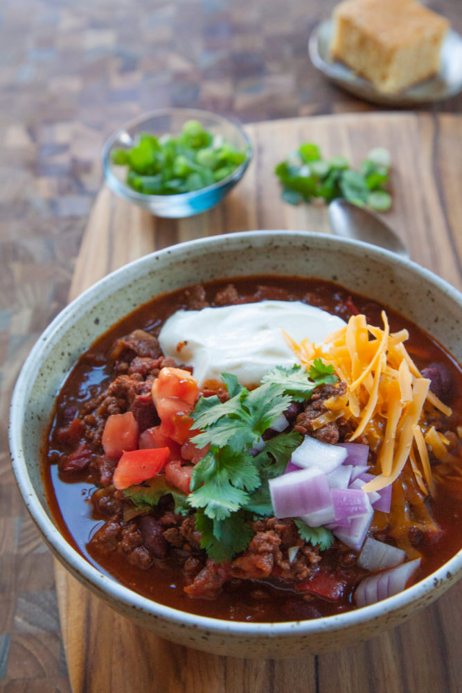 A bowl of chili with sour cream, cheese, green onions and tomatoes on top. 