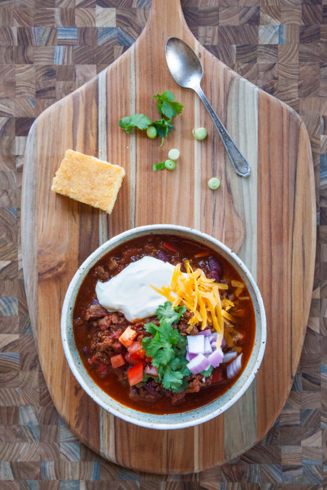 A bowl of chili with sour cream, cheese, green onions and tomatoes on top.