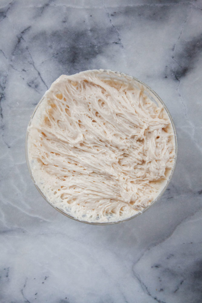 Bread sponge in a bowl, after it's rested and the gluten has formed, appearing stringy and sticky.