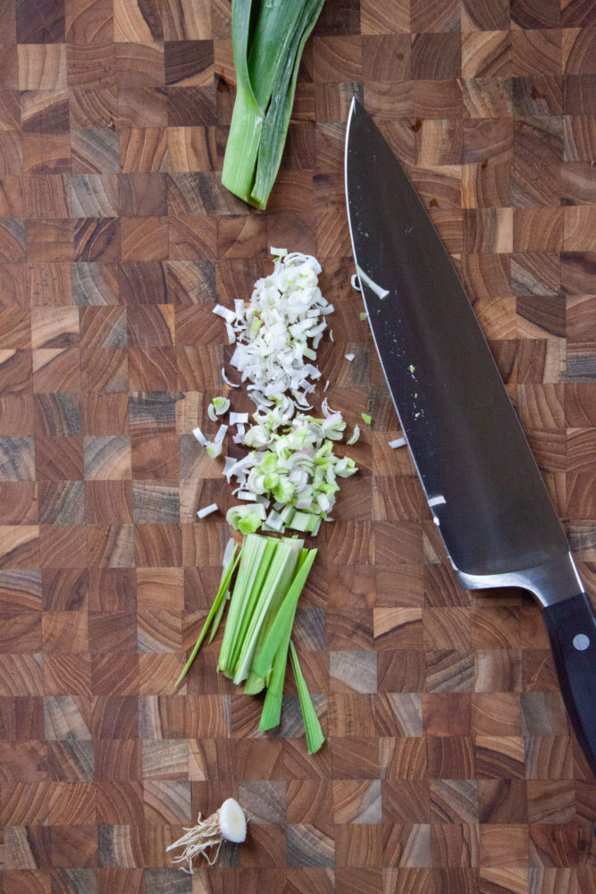 Green garlic, sometimes called wet garlic, chopped on a wooden cutting board.