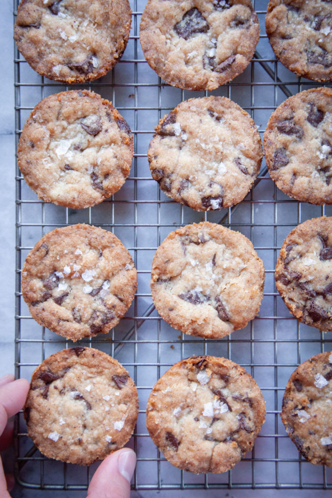 A hand reaching for chocolate chip shortbread cookies on a wire cooling rack.