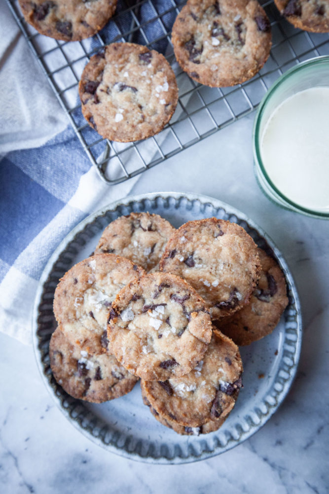 Stacks of chocolate chip shortbread cookies on a plate, with more cookies on a wire rack next to it.