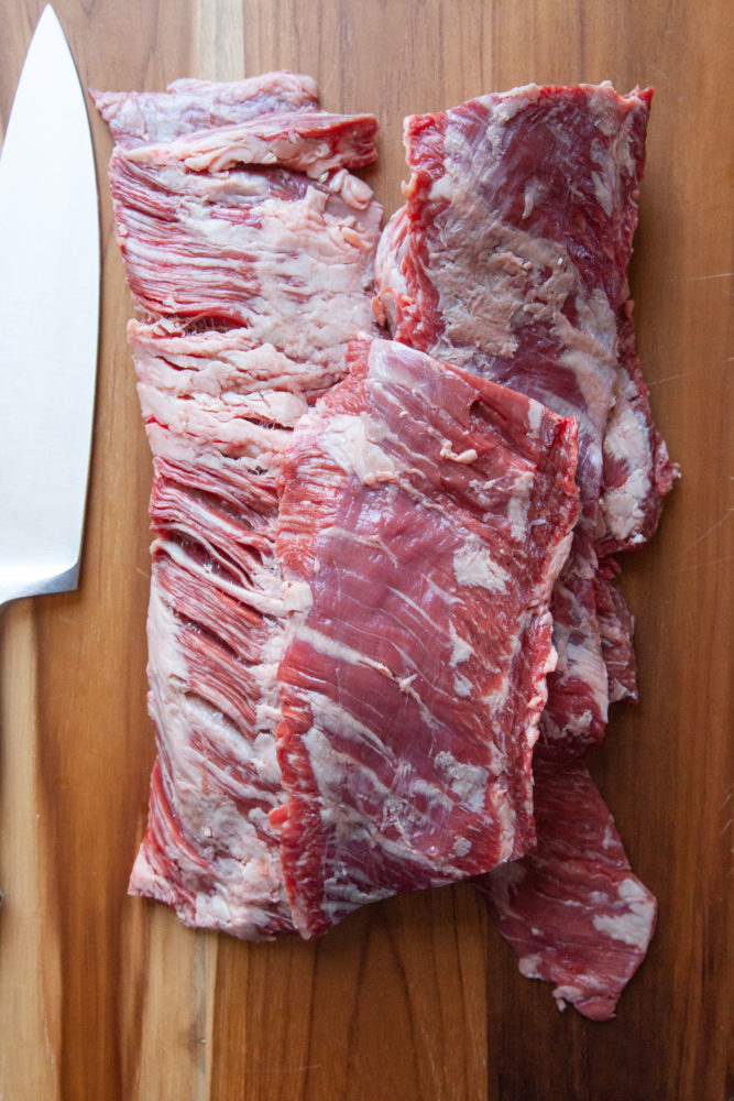 Pieces of skirt steak cut on a cutting board with a chef knife next to it.