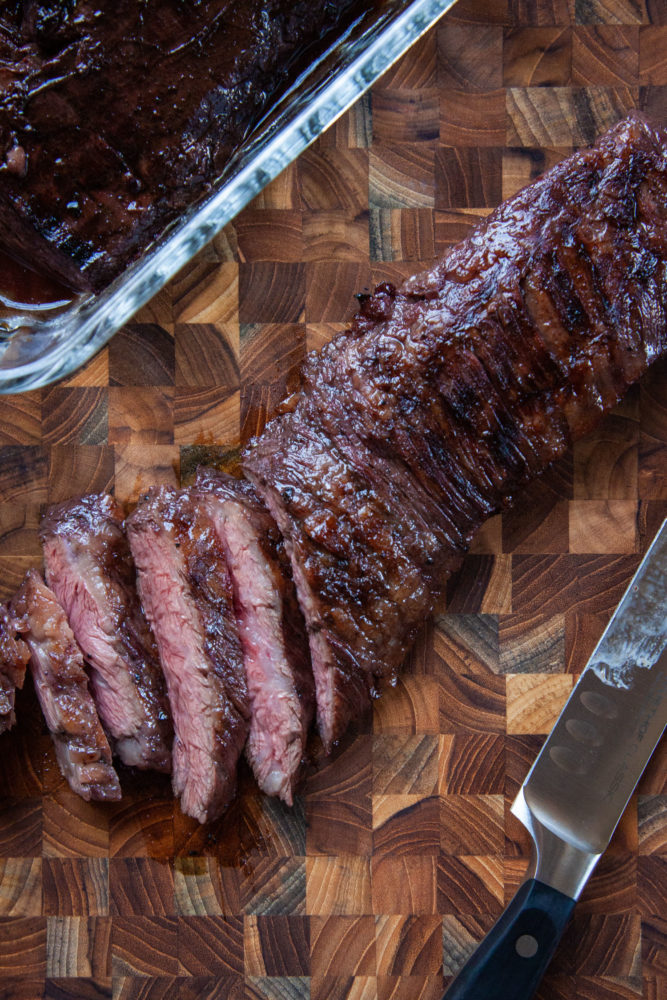 Sangria-inspired marinade grilled skirt steak sliced on a cutting board with a carving knife next to it.