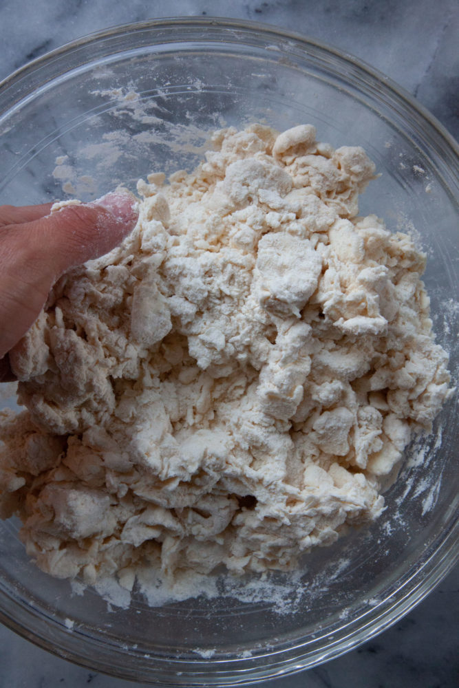 A hand smashing the butter in a bowl with flour and salt, making the pie dough.