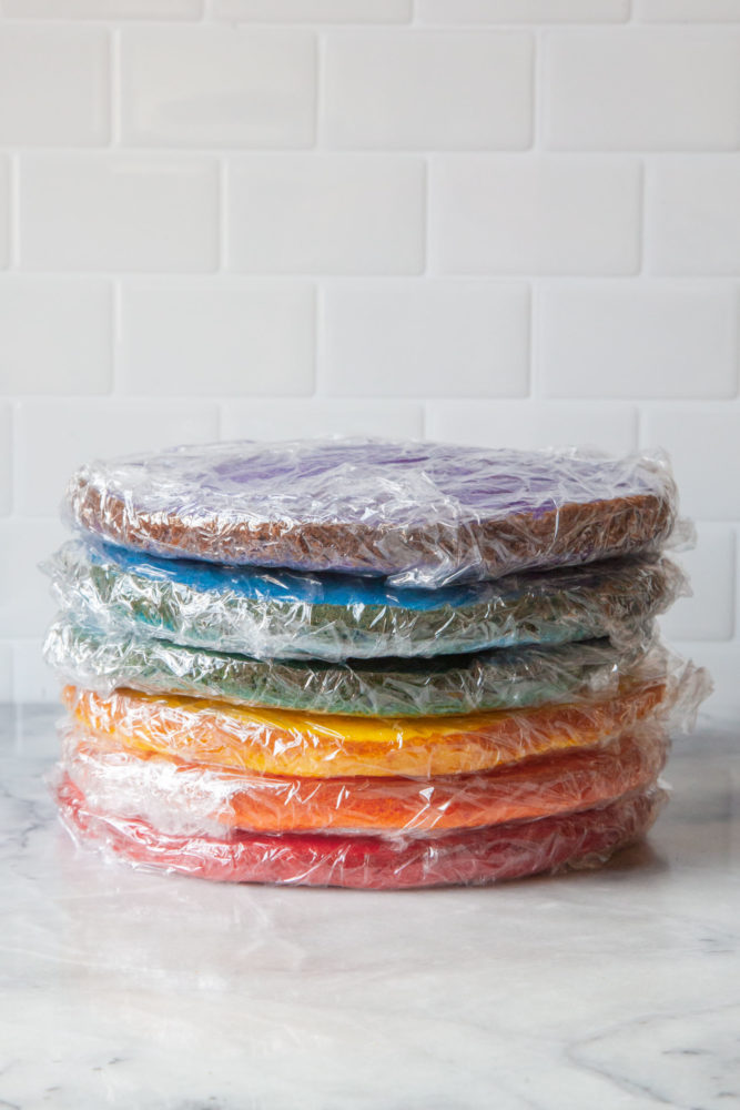 A stack of different colored layer cakes wrapped plastic wrap so they can be frosted the next day.