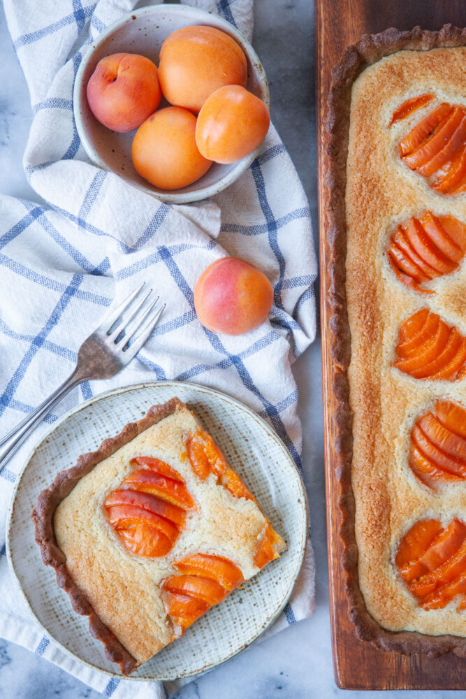 A slice of apricot frangipane on a plate, with the remaining tart next to it.