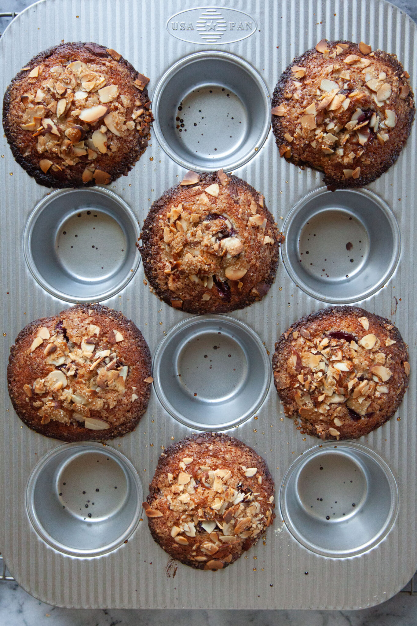 A muffin pan with baked cherry almond muffins alternating in every other muffin cup.