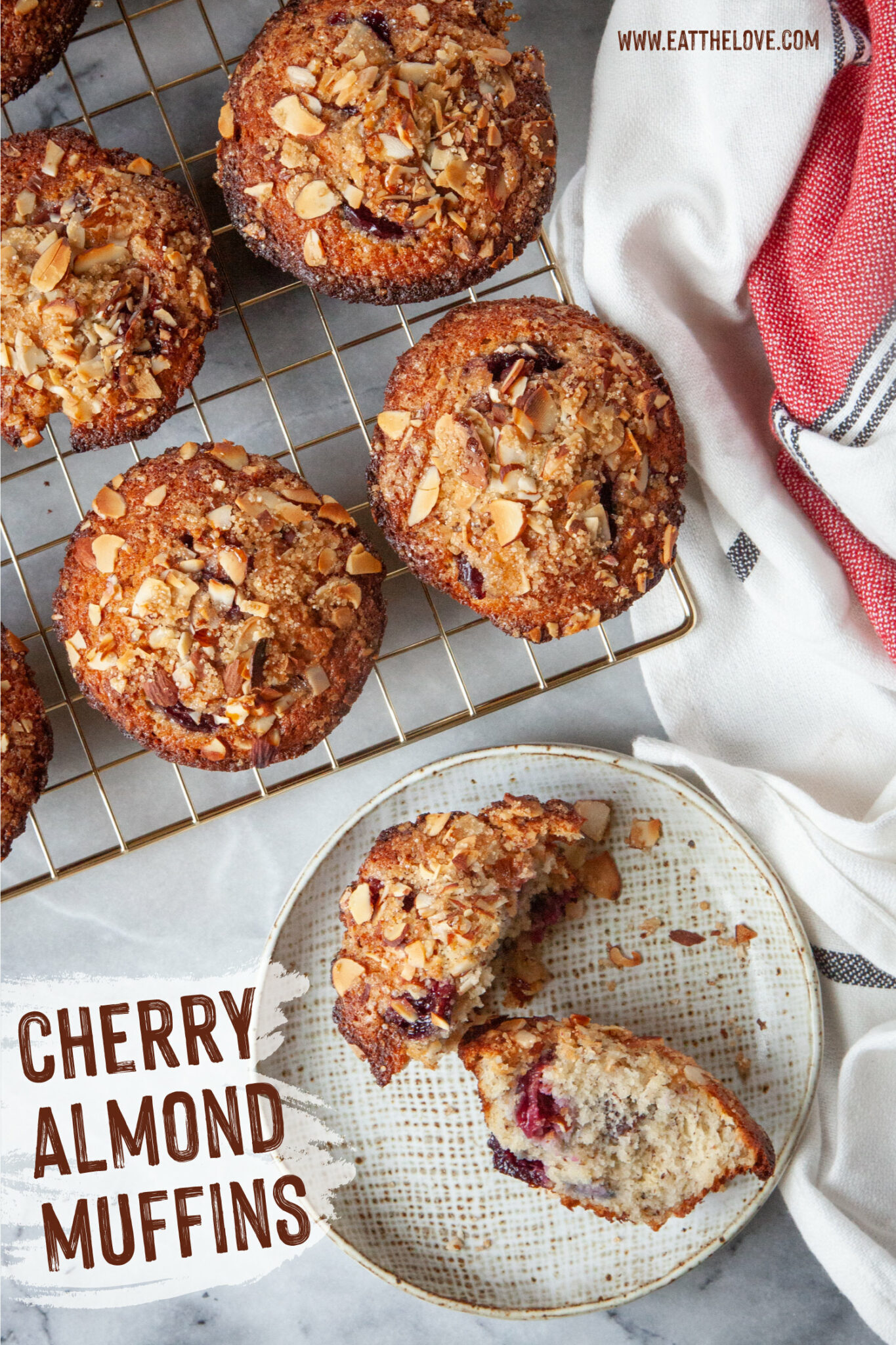 A cherry almond muffin split in half on a plate, with more muffins on a wire rack next to it.