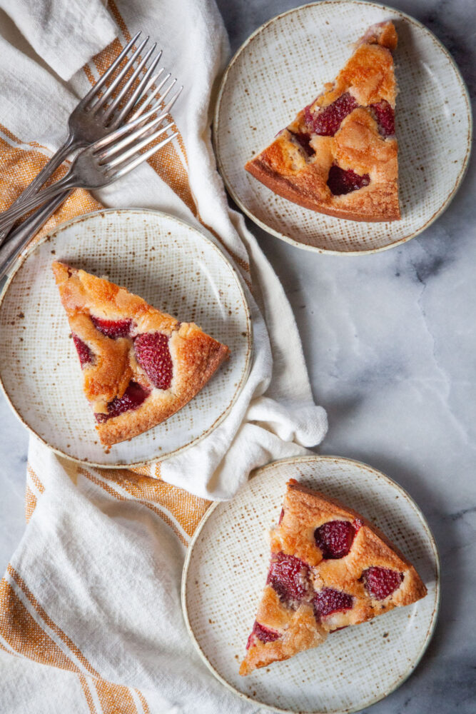 Three slices of strawberry cake on three small plates.