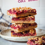 A stack of raspberry oat bars on a plate, with one more raspberry oat bar on the table in front of it.