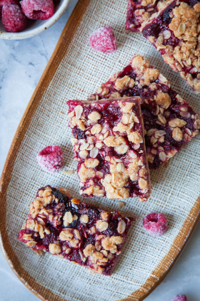 Some raspberry oat bars on a plate, with frozen raspberries next to them.