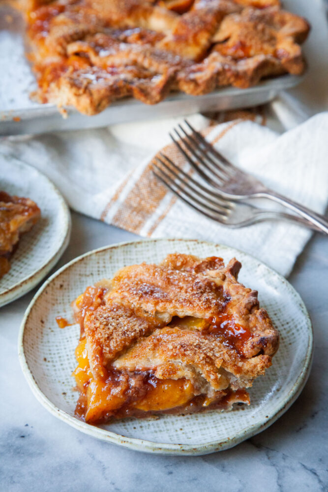 A slice of peach slab pie on a plate, with more pie behind it.