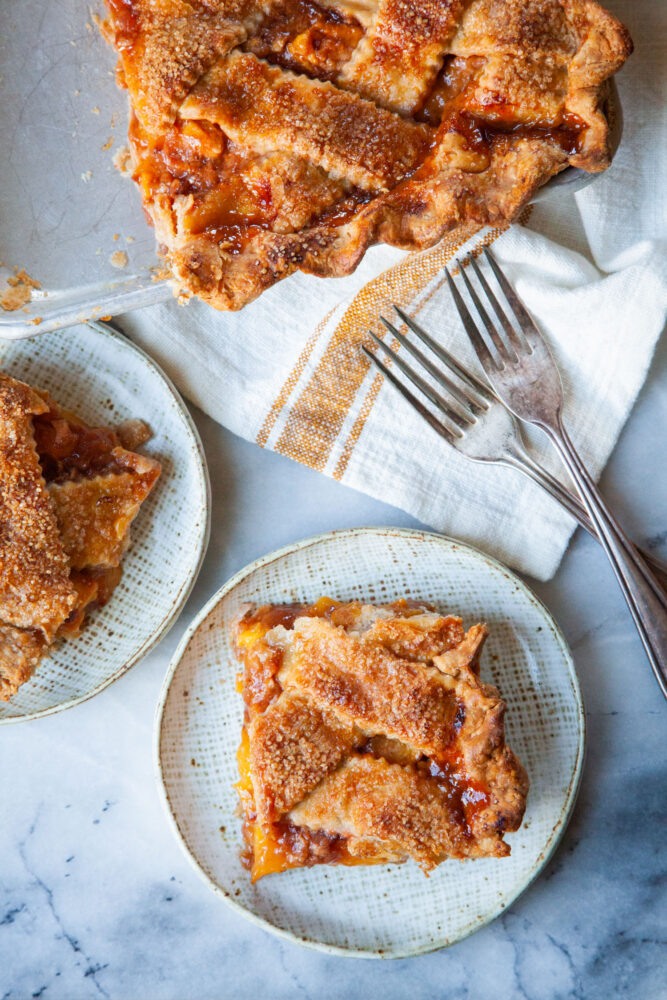 Two slices of peach slab pie on a plates, with the remaining pie next to them.