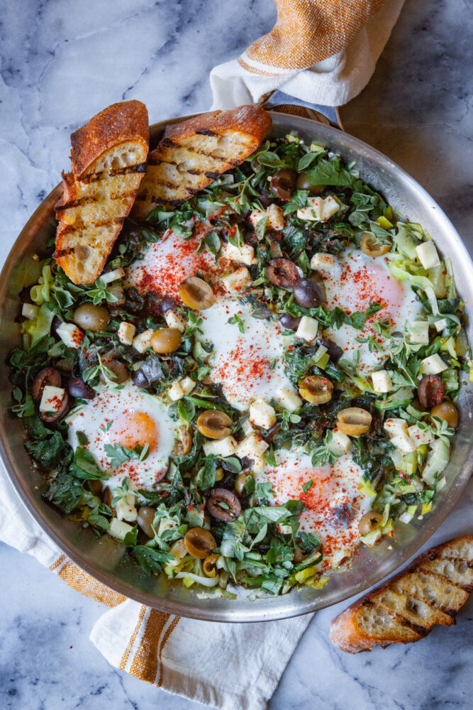 A pan of green shakshuka with toast tucked into the edges of the pan.